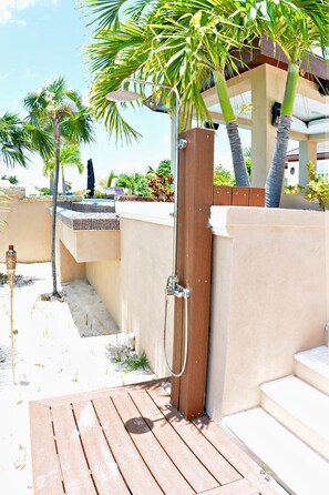 Um deck de madeira que dá para uma área de piscina, com um portão de madeira, palmeiras e uma piscina revestida em azulejo.