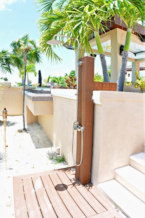 Eine Holzterrasse führt zu einem Poolbereich mit einem Holztor, Palmen und einem gefliesten Pool.