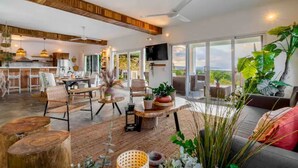 A spacious living area with a large window, a ceiling fan, and a dining area with wooden furniture.
