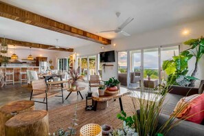 A spacious living area with a large window, a ceiling fan, and a dining area with wooden furniture. - VeoMar-Casita Xander: villa de 3 dormitorios con vistas panorámicas (Rio San Juan)