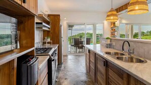 A modern kitchen with a stove, oven, and sink, wooden cabinets, and a view to a patio area.
