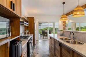 A modern kitchen with a stove, oven, and sink, wooden cabinets, and a view to a patio area. - VeoMar-Casita Xander: villa de 3 dormitorios con vistas panorámicas (Rio San Juan)