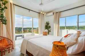 A bedroom with a large bed, a hanging chair, a bedside table, and a view of a balcony with plants and flowers. - VeoMar-Casita Xander: villa de 3 dormitorios con vistas panorámicas (Rio San Juan)