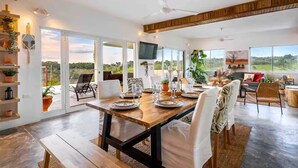 A spacious dining area with a wooden table set for a meal, large windows offering a view of the outdoors, and a ceiling fan.