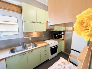 A compact kitchen with a sink, stove, microwave, and a single refrigerator. - Urban Escape With Acropolis View by MPS (Athina)