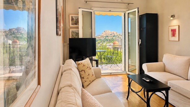 Un salon comprenant un canapé, un téléviseur, un balcon avec vue sur une montagne et une porte donnant sur un espace extérieur.