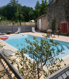 Piscina con sillas de descanso y una mesa, rodeada de follaje y un edificio de piedra.