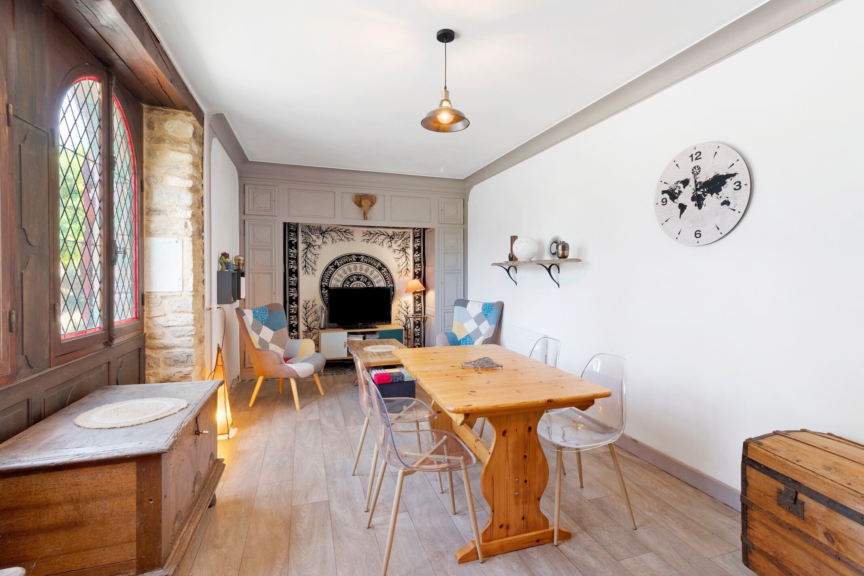 A dining area with a wooden table, chairs, a world map clock, and a stone wall.