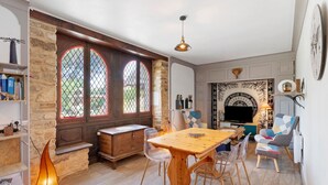 A dining area with a wooden table and chairs, a stone wall, and a fireplace with a decorative mantle. - La Maison Dô – Stone House with Pool for 4 Guests Near Dordogne (Frayssinet-le-Gélat)