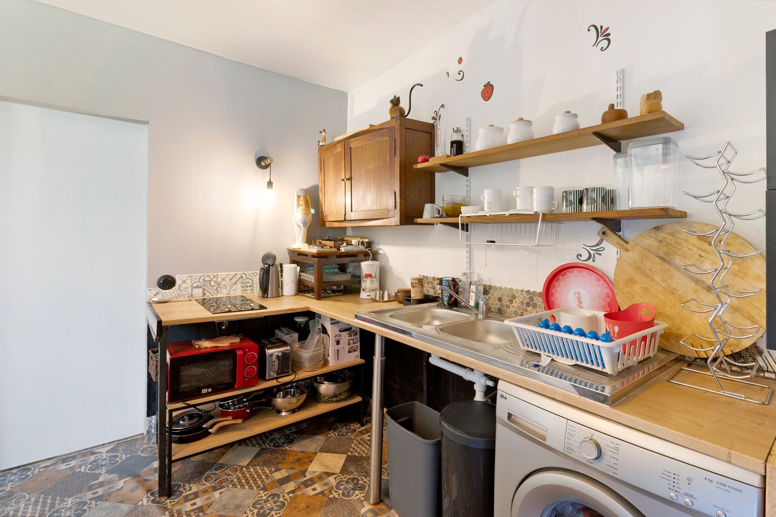 Una cocina compacta con lavadora, estantes con vajilla y microondas.