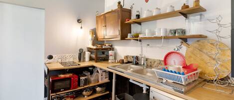 Una cocina compacta con lavadora, estantes con vajilla y microondas.