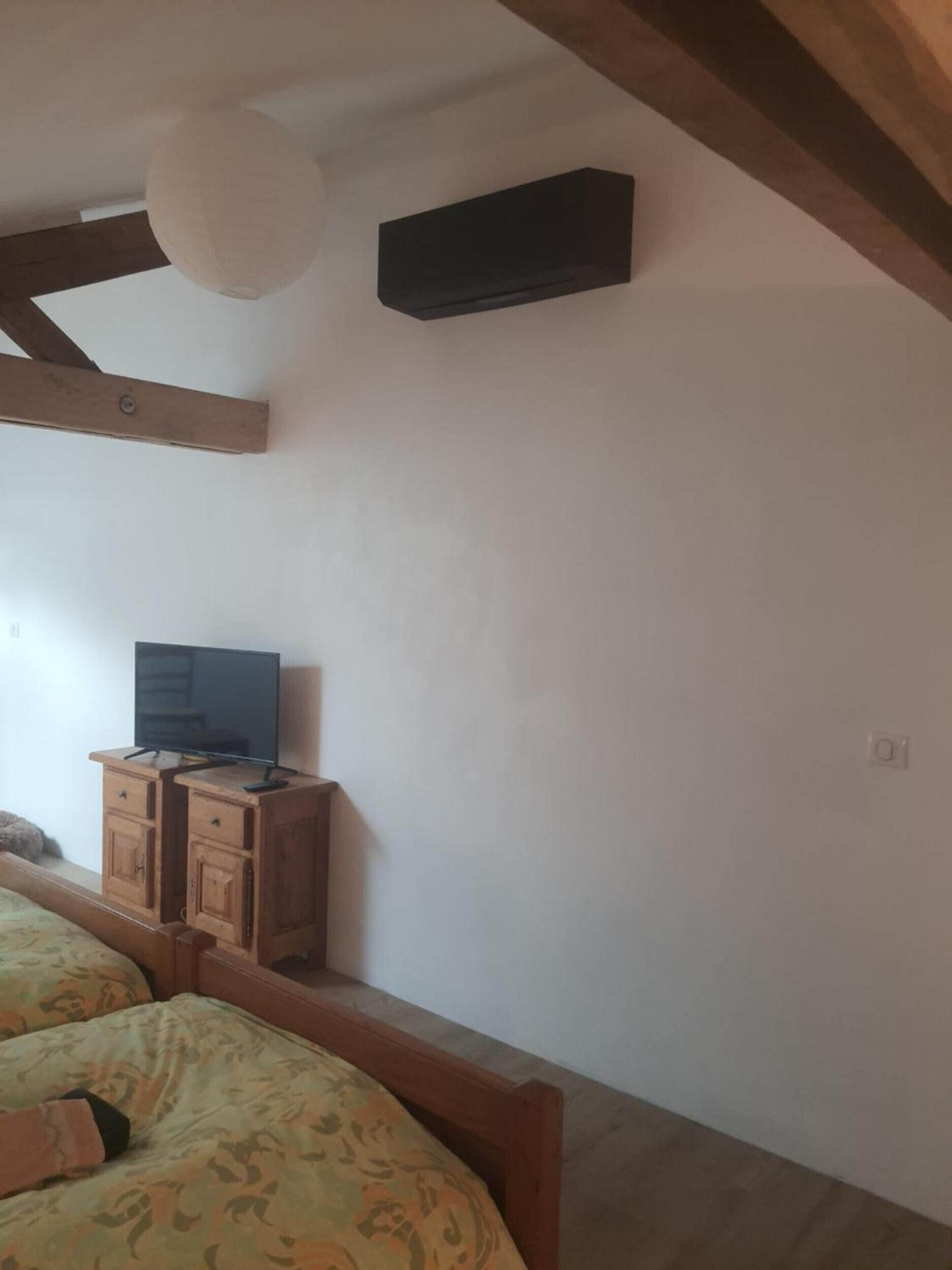 Une chambre à coucher avec un lit, un téléviseur posé sur un meuble en bois et un ventilateur de plafond.