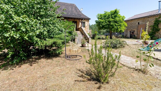 Een stenen huis met een schotelantenne, een trap en een tuin met verschillende planten en een schommel.