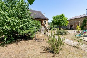 Ein Steinhaus mit Satellitenschüssel, einer Treppe und einem Garten mit verschiedenen Pflanzen und einer Schaukel.