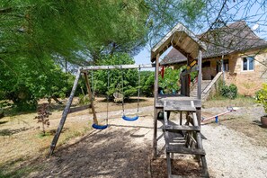 Un columpio de madera, una pequeña construcción de madera y una casa en un jardín.