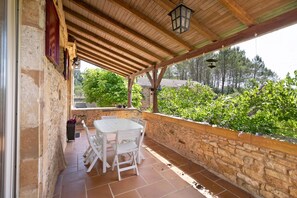 Eine überdachte Terrasse mit Steinwand, Tisch und Stühlen sowie Blick auf Grünflächen.