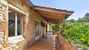 Un edificio de piedra con un porche techado, una mesa y sillas, y una ventana.