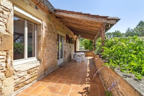 A stone building with a covered patio, a table and chairs, and a window.