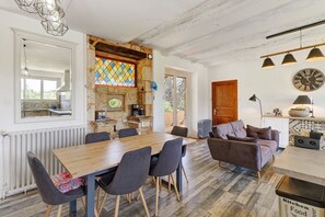 A spacious kitchen with a wooden table and chairs, a stone wall with a stained glass window, and a rustic ceiling.