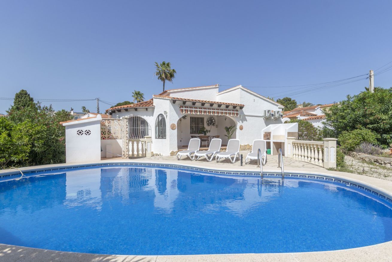 A poolside area with a pool, lounge chairs, and a building with a tiled roof.