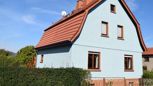 A light blue house with a red roof, multiple windows, and a satellite dish.