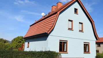 Ein hellblaues Haus mit rotem Dach, zahlreichen Fenstern und einer Satellitenschüssel.