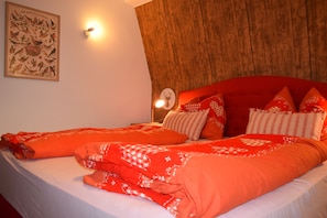 Un lit avec une literie rouge, une tête de lit en bois, une lampe fixée au mur et une affiche encadrée.