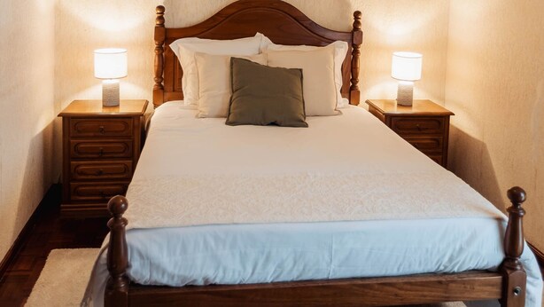 Een slaapkamer met een houten bed, twee nachtkastjes met lampen, een hanglamp en een kunstwerk aan de muur.
