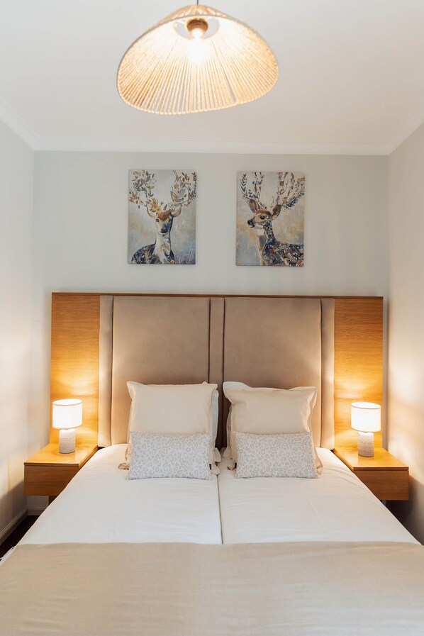 Un lit double avec deux oreillers, une tête de lit, des lampes de chevet et deux tableaux représentant des cerfs, accrochés au mur.