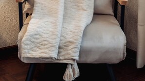 A chair with a textured blanket and tassels, wooden armrests, and black legs. - Villa Views_Double Room with Extra Bed 25 (Cabeceiras de Basto)