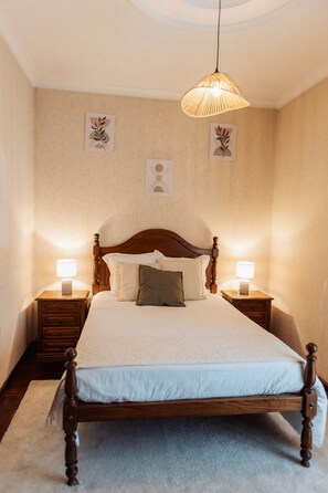 A bedroom with a wooden bed, two bedside tables with lamps, a hanging light fixture, and wall art. - defaultName (Cabeceiras de Basto)