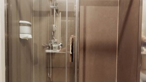 A glass-enclosed shower stall with a handheld showerhead, a wall-mounted soap dispenser, and a visible towel rack.