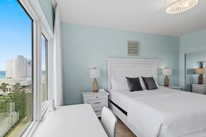 A hotel room with a large bed, two bedside tables, a nightstand, a view of the city, and a window with curtains. - 🌴Summit at Tops'l 612 | Large Balcony with Gulf Views | Pool | Walk to Beach🌞 (Miramar Beach)