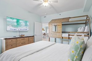 Ein Schlafzimmer mit einem Etagenbett, einem Deckenventilator, einem an der Wand montierten Fernseher und einer hölzernen Kommode.