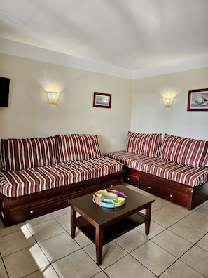 A living room with two striped sofas, a coffee table, wall-mounted lights, and framed pictures. - Apartment for 7 in the Heart of Biscarrosse Golf – Pool, Nature & Relaxation (Biscarrosse)