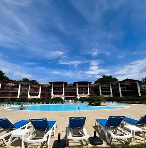 A pool area with lounge chairs and a building with balconies. - Apartment for 7 in the Heart of Biscarrosse Golf – Pool, Nature & Relaxation (Biscarrosse)