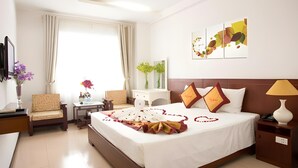 A hotel room with a large bed, a desk, a chair, a TV, and a window with curtains. - Star Hotel (Da Nang)