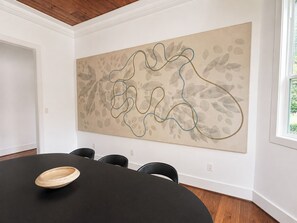 A conference room with a large abstract painting on the wall, a black table with a wooden bowl, and a window with a view of greenery. - New! Montrose Art Bungalow + Private Gallery Tour (Houston)