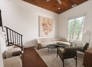 Uma sala de estar com teto de madeira, uma janela grande, um sofá, uma mesa de centro e um quadro na parede.