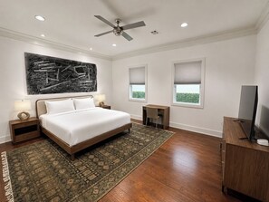 A bedroom with a bed, a ceiling fan, a desk, a TV, and a large abstract painting on the wall. - New! Montrose Art Bungalow + Private Gallery Tour (Houston)