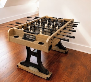 Ein Kicker mit Holzfüßen, der auf einem Holzboden vor einer weißen Wand steht.