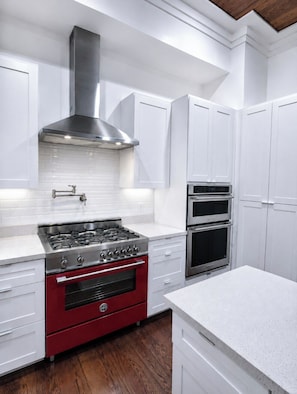A kitchen with white cabinetry, a red oven, a stainless steel range, and a double oven. - New! Montrose Art Bungalow + Private Gallery Tour (Houston)