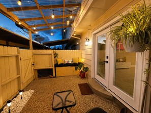 Ein überdachter Patio-Bereich mit Sitzgelegenheit, einem Glastür-Eingang und Lichterketten.