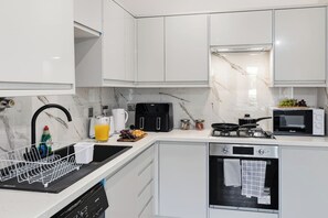 Een moderne keuken met witte kasten, een zwarte kraan, een koffiezetapparaat, een broodrooster, een magnetron en een vaatwasser.