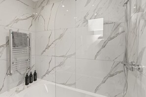 A bathroom with a marble wall, a shower, a bathtub, and a towel rack with a towel. - Families | Free Parking | Links to Manchester (Greater Manchester)