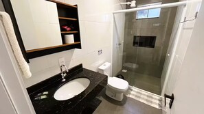 Een badkamer met een zwart marmeren wastafel, toilet in het wit en een douche met glazen wanden.