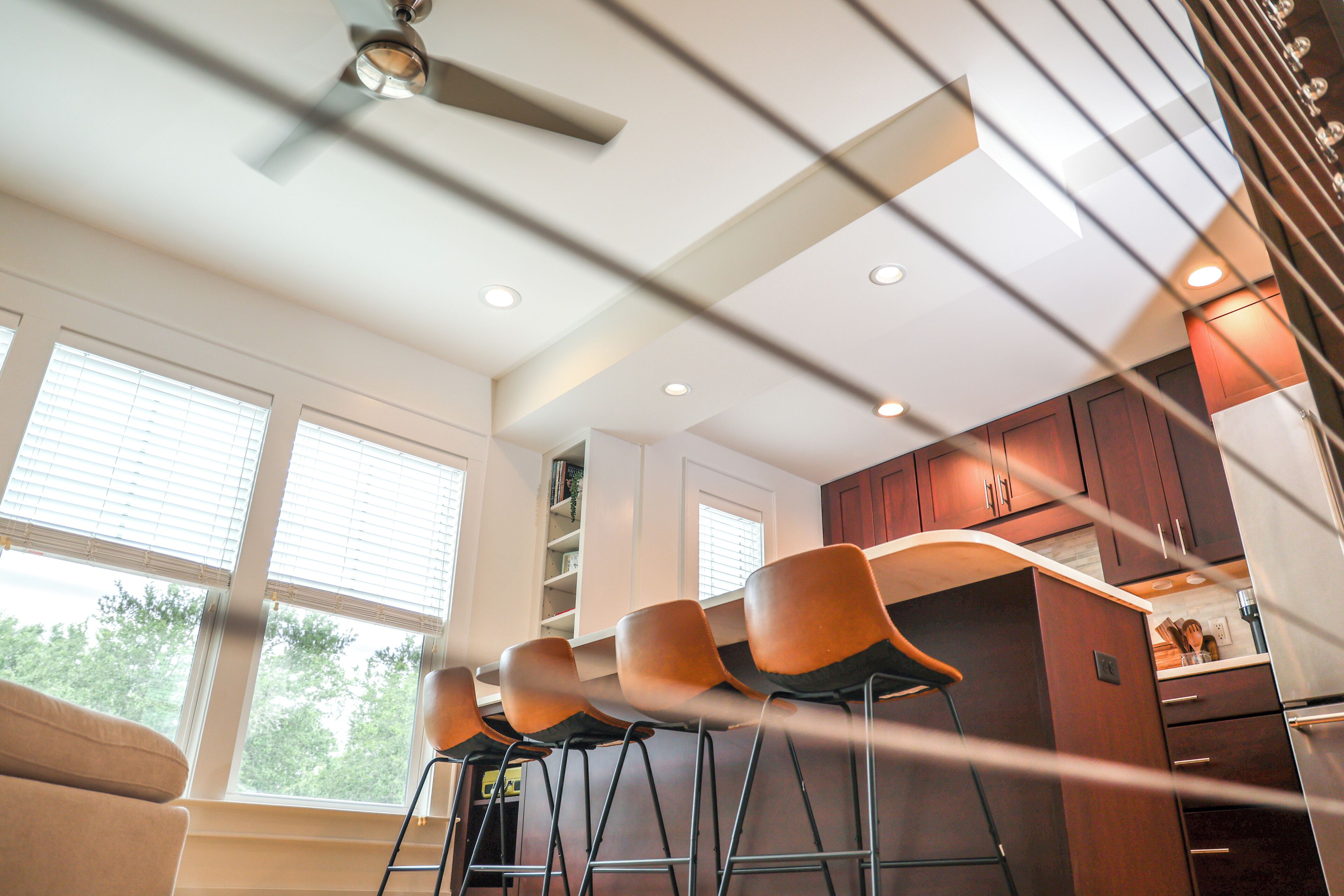 A modern kitchen with bar stools, a ceiling fan, and wooden cabinets.