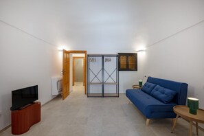 Ein gemütlicher Wohnraum mit Fernseher auf einem Holzständer, einem blauen Sofa, einem kleinen Tisch mit einer grünen Tasse und einem Kleiderschrank mit Spiegel.