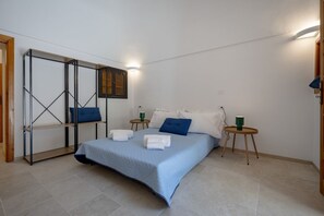 Ein Schlafzimmer mit einem Bett, Kissen, einem Nachttisch, einem an der Wand montierten Fernseher und einem Holzregal.