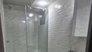 A bathroom with a glass-enclosed shower, a toilet, a sink, and a mirror.